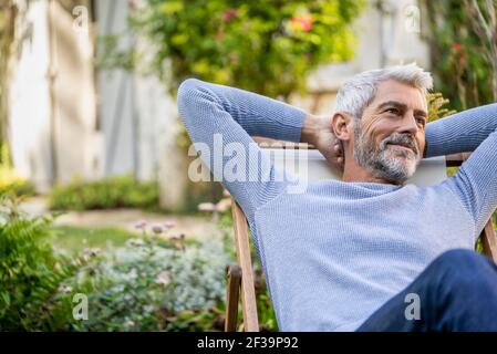 Uomo maturo sorridente con le mani dietro la testa seduta su sdraio Foto Stock