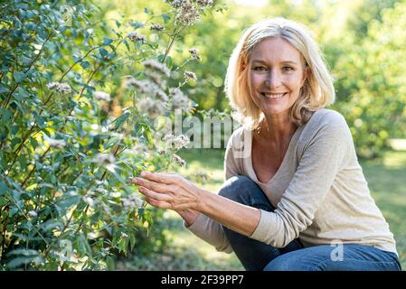 Ritratto di donna matura sorridente che tocca la pianta in cortile Foto Stock