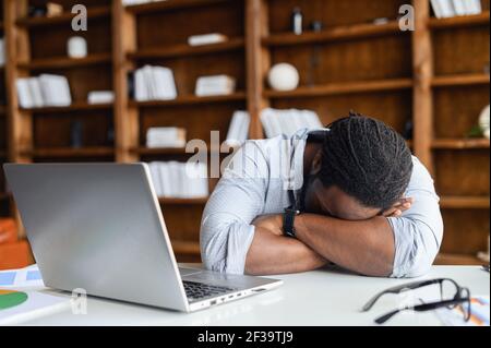 Afro-americano stanco privato uomo d'affari sensazione di mancanza di sonno avendo pisolino sul posto di lavoro, nero inquieto imprenditore disperato da fallimento o debito, depresso investitore disperato in caso di fallimento Foto Stock