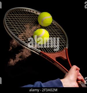 La racchetta da tennis colpisce due palline gialle che lasciano un sentiero di polvere rossastra Foto Stock