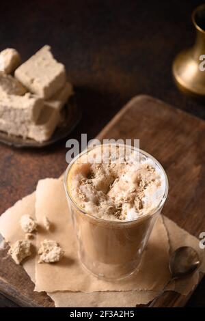 Gustoso latte di caffè fatto in casa con alva in tazza di vetro su sfondo marrone scuro. Primo piano. Foto Stock