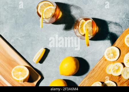 vista dall'alto dei bicchieri con cocktail alcolico e limone accanto ai limoni sulle tavole su sfondo grigio Foto Stock