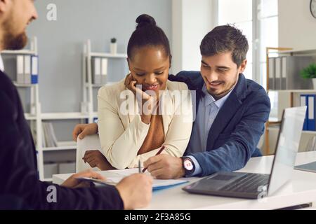 Felice coppia interracial firma le carte dopo consultazione con il consulente personale Foto Stock