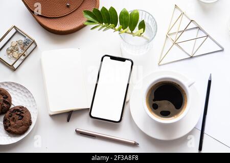 Piano da tavolo bianco per l'ufficio domestico con mock-up per smartphone, tazza da caffè e blocco note Foto Stock