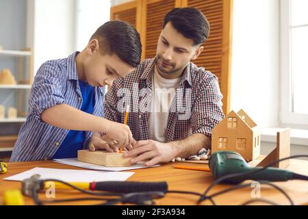 Il carpentiere del padre che si prende cura nel laboratorio insegna al figlio poco interessato di fare una casa di legno. Foto Stock