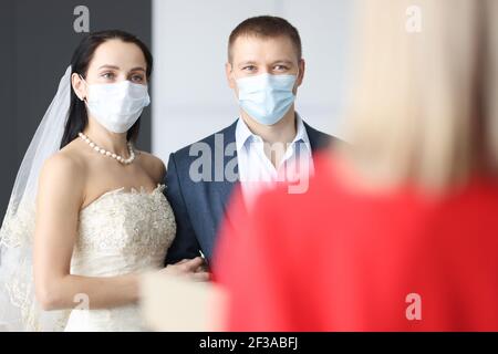 Sposa e sposo che indossano maschere mediche di protezione in piedi davanti di receptionist Foto Stock