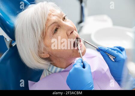 Ortodontista che raggiunge la bocca della donna anziana con gli attrezzi Foto Stock