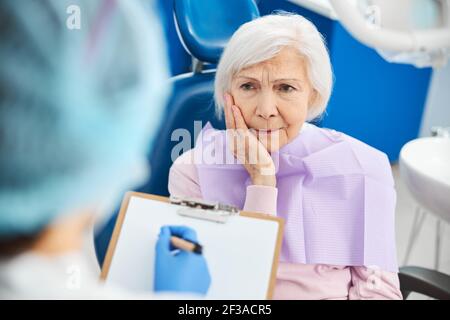 Donna in pensione sentendo dolore ai denti e informando il dentista Foto Stock