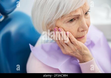 Triste età femmina afferrare la sua guancia a causa di mal di denti Foto Stock