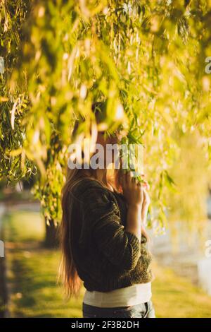 Foto di ragazza elegante in piedi tra i rami salici in un tramonto d'oro Foto Stock