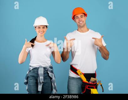 Scegliete noi per la riparazione. Due operatori di Handycam felici in Hardhats che si indicano Foto Stock