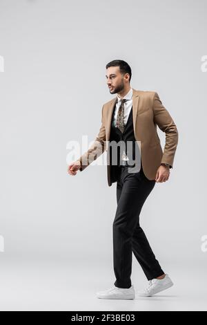 vista completa dell'uomo musulmano alla moda in tuta e. sneakers che camminano sul grigio Foto Stock