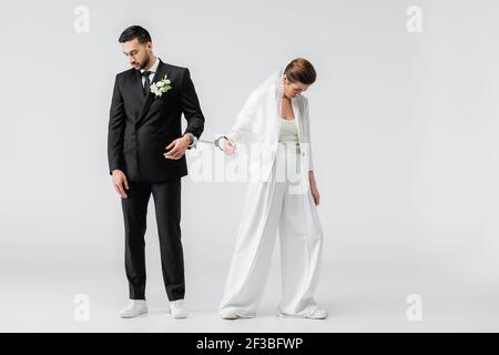 Triste sposo interrazziale e sposa in manette su sfondo bianco Foto Stock