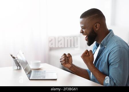 L'uomo freelancer afro-americano è stato molto felice di guardare il notebook e di fare il tifo operazione riuscita Foto Stock