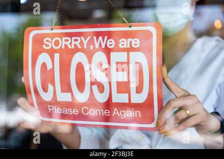 donna asiatica che indossa maschera di protezione volto girando cartello chiuso su porta di vetro per il ristorante open cafe dopo coronavirus o covid-19 quarantena. re Foto Stock