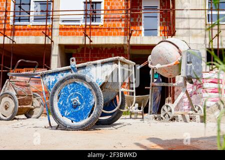 Carriola obsoleta industriale usata collocata in cantiere, impalcatura posta contro l'edificio in costruzione per esigenze logistiche. Foto Stock