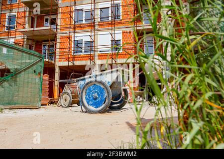 Carriola obsoleta industriale usata collocata in cantiere, impalcatura posta contro l'edificio in costruzione per esigenze logistiche. Foto Stock