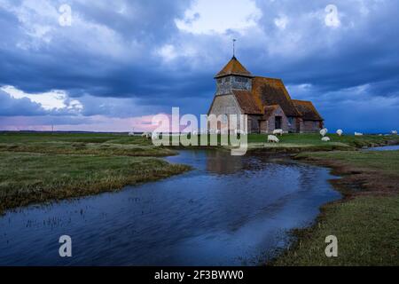 Chiesa di San Thomas Becket vicino a Fairfield sulla Marsh Romney nel Kent, Inghilterra sud-orientale, nubi tempesta che si radunano durante l'ora blu e pascolo delle pecore Foto Stock