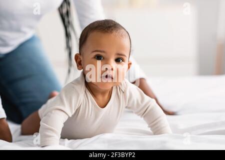 Carino piccolo afroamericano bambino strisciando a letto Foto Stock