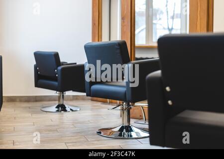 Salone di bellezza interno barbiere. Comode poltrone in pelle nera di fronte a grandi specchi panoramici con eleganti cornici in legno in stile moderno Foto Stock