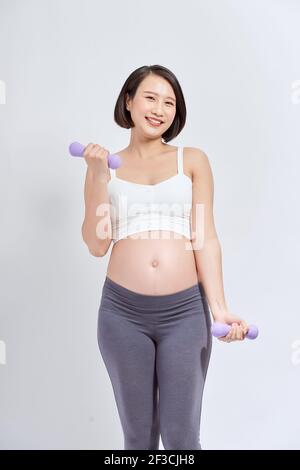 Donna incinta asiatica fare esercizio, in piedi e sollevando dumbbells, concetto di maternità di gravidanza sportiva Foto Stock