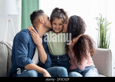 Amore per la famiglia. I genitori premurosi Kissing loro figlia piccola, legandosi insieme a casa Foto Stock