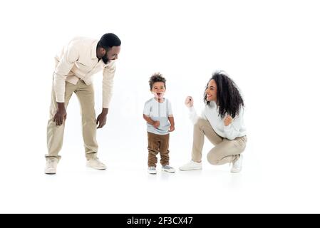 eccitata donna afroamericana mostrando il gesto di vittoria vicino stupito figlio e felice marito su bianco Foto Stock