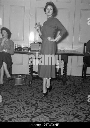 1957, storica, elegante giovane donna in un elegante vestito dell'epoca in un ufficio festa in una sala con un bicchiere di vino, Victoria Hotel, Leeds, Inghilterra. REGNO UNITO. Foto Stock