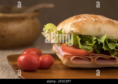 Una foto ravvicinata di un sandwich di prosciutto con pane di ciabatta, lattuga e pomodori su un tagliere. Foto Stock