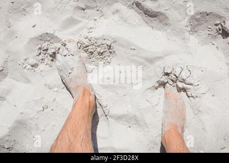 Le gambe del giovanotto si trovano distese sulla sabbia bianca della spiaggia, la vista dall'alto. Foto Stock