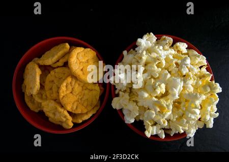 Chiudi Vista dall'alto di Popcorn e chip di riso al barbecue In ciotole rosse isolate su nero orizzontale Foto Stock