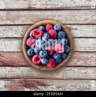 Vista dall'alto. Bacche blu e rosse nel recipiente. Lamponi e mirtilli maturi su sfondo ligneo. . Sfondo di frutti di bosco misti con spazio per la copia del testo. Foto Stock