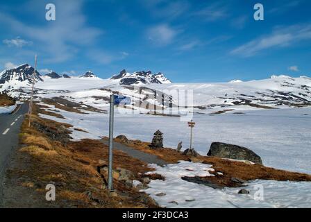 Norvegia, strada sgorgata e cartelli per piste ciclabili e sentieri escursionistici al passo Sognefjell in tarda primavera Foto Stock