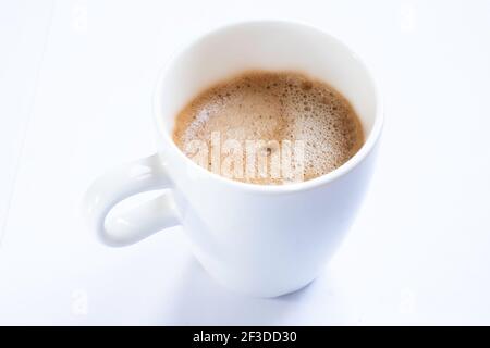 Tazza di caffè con manico, isolata su un tavolo bianco. Vista obliquamente dall'alto. Mettere a fuoco la schiuma del caffè. Tazza senza piatto Foto Stock
