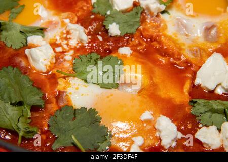 Una deliziosa pentola di Shakshuka con avocado e uova di harissa bollire in una padella grande Foto Stock