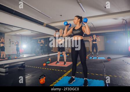 Gruppo di giovani donne atletiche in abbigliamento sportivo con manubri in esercizio in palestra Foto Stock