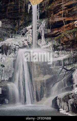 Cascata panoramica e bellissima con le sue ghiacciate sui lati che si gettano su una scogliera umida e rossa ricoperta da muschio colorato Foto Stock