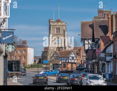 Pinner Village High Street con la chiesa parrocchiale di San Giovanni Battista, negozi, auto parcheggiate e tre giovani uomini a piedi sul marciapiede. NW London, Inghilterra Foto Stock