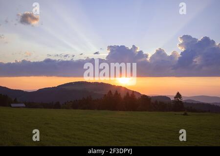 Incredibile cielo al tramonto sopra le montagne del Giura, Svizzera. Splendido paesaggio nuvoloso con raggi di sole visibili e luce sulle colline e sul campo Foto Stock