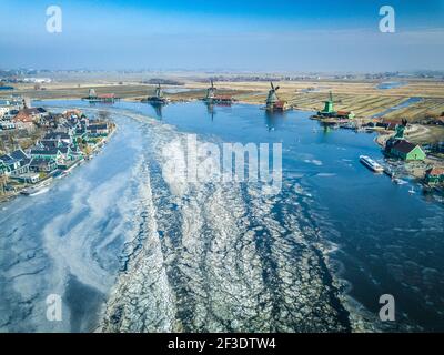 Vista del drone sulla svolta del fiume con superficie coperta da galleggianti galleggianti di ghiaccio. Colorati mulini a vento e case sulle rive del fiume. Foto Stock