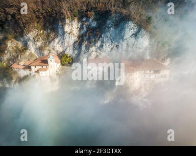 Vista aerea su diverse case incastrate sulla parete rocciosa. Il sole splende sui tetti sopra la nebbia sparsa. Atmosfera Moody. Foto Stock