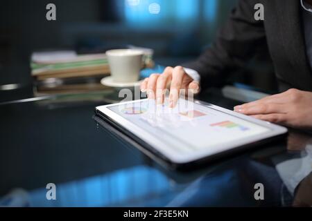 Primo piano di un tele worker che controlla i grafici online su un tablet in tarda ora a casa Foto Stock