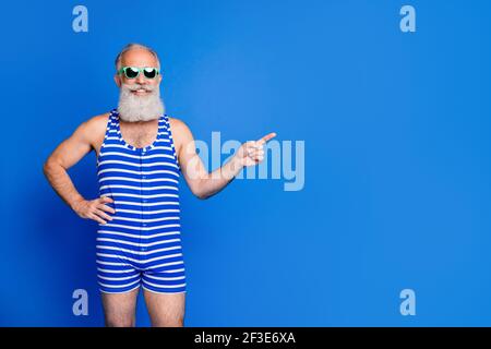 Foto di bello positivo sorridente maturo uomo punto copyspace dito pubblicità isolata su sfondo blu Foto Stock