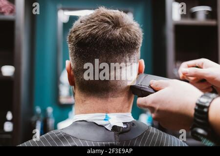 Vista posteriore processo di taglio uomo, cliente seduto in sedia barbiere e parrucchiere radersi i suoi capelli con il regolacapelli. Foto Stock