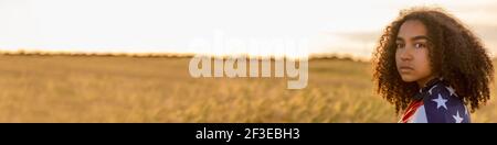 Panorama triste depresso misto razza Africana americana ragazza adolescente femmina giovane donna in un campo di grano o coltivazioni di orzo Avvolto in stelle e strisce USA Foto Stock