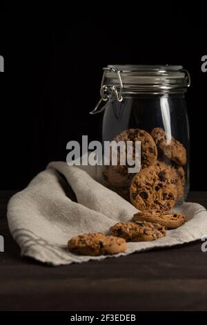 Vista del vaso di vetro con biscotti su tela su tavola di legno, su fondo nero, in verticale, con spazio per la copia Foto Stock