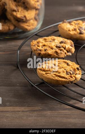 Vista dall'alto dei biscotti al cioccolato su scaffale nero e vasetto di vetro, a fuoco selettivo, su tavolo di legno, in verticale Foto Stock