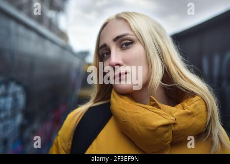 Primo piano ritratto di ragazza teen hipster bionda che fa selfie, sta indossando giacca gialla e zaino, camminando all'aperto attraverso il passaggio sotterraneo Foto Stock