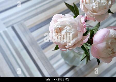 Un bouquet di peonie in un vaso di vetro trasparente. Peonie rosa e bianche sul tavolo ricoperte da stuoie a motivo Foto Stock