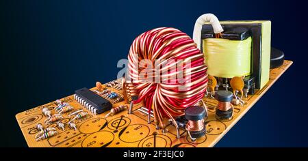 Componenti elettronici nella scheda a circuito stampato arancione che volano su sfondo blu scuro. Scena astratta. Bobine con nucleo in ferrite, resistori, chip, trasformatore su circuito stampato. Foto Stock